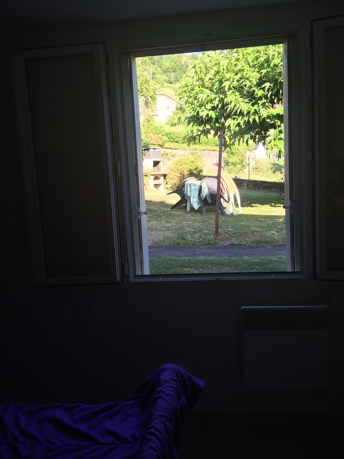 A view from an interior window reveals a tranquil garden space. The area features a tree and is decorated with colorful items hanging on a line. The surrounding greenery adds a serene touch to the outdoor setting.