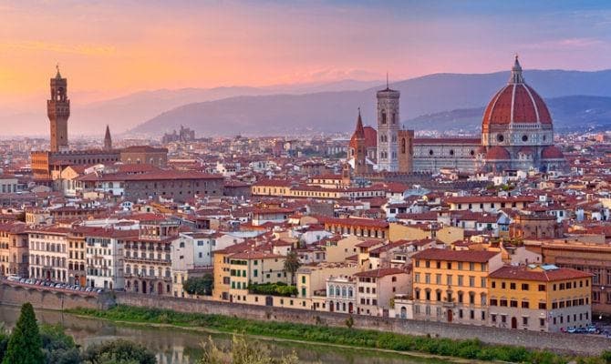 A panoramic view of Florence during sunset is displayed, featuring the iconic dome of the Cathedral of Santa Maria del Fiore. The historic buildings and rooftops are bathed in warm hues, while the Arno River gently reflects the evening light.