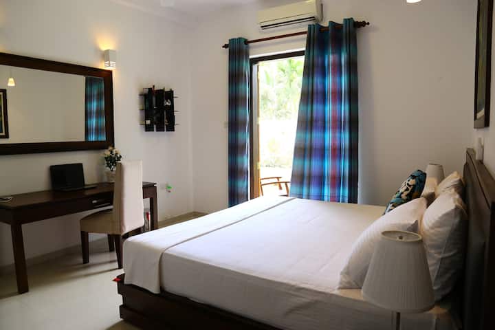 - Bright villa bedroom with blue curtains and outdoor view  
- Perfect tropical stay in Sri Lanka for families and couples  
- Spacious retreat with modern furnishing and natural light  
