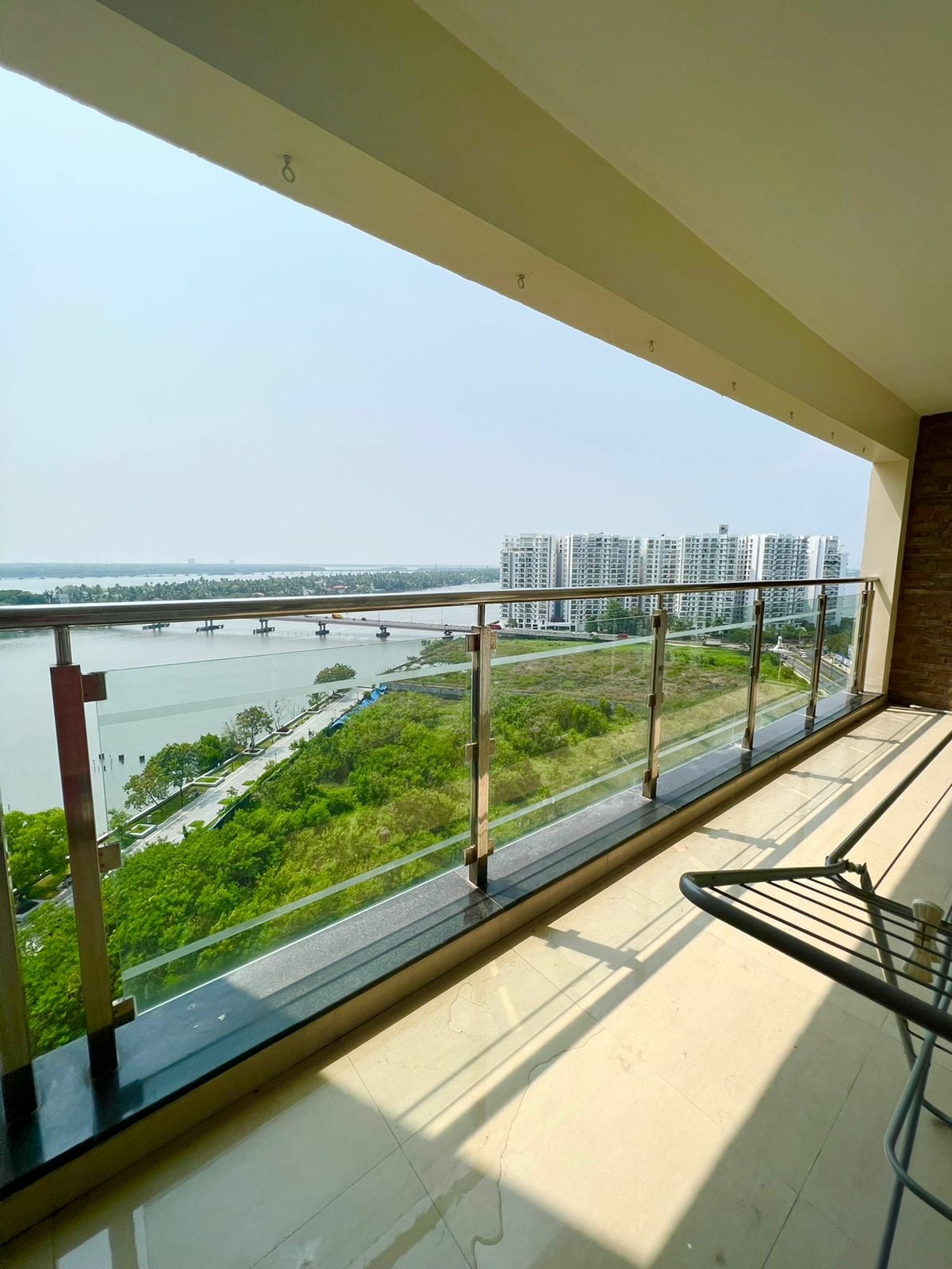A panoramic view is captured from a spacious balcony, showcasing the serene waterfront and lush greenery below. The glass railing offers an unobstructed sightline of the nearby buildings and bridges, creating a bridge between indoor comfort and the outdoor landscape.