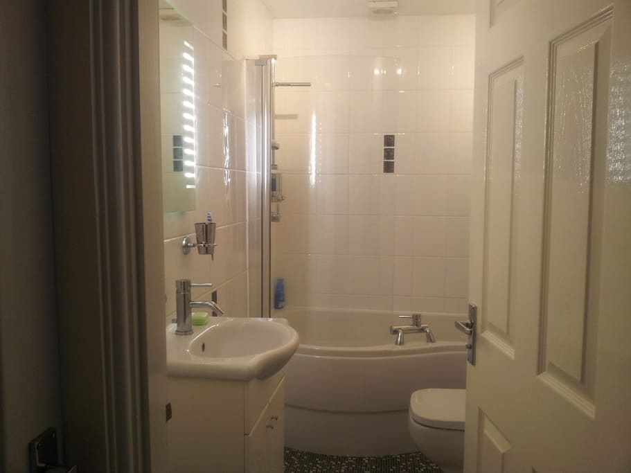 Compact modern heated bathroom with curved bath & overhead shower