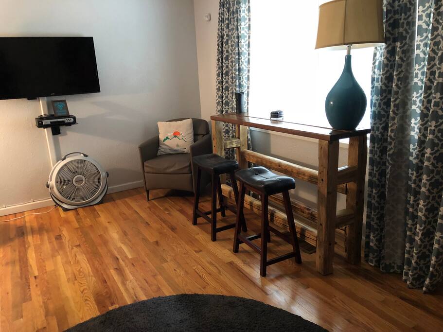 The living room has a custom bar top table with stools, a flat screen tv and leather sofa.