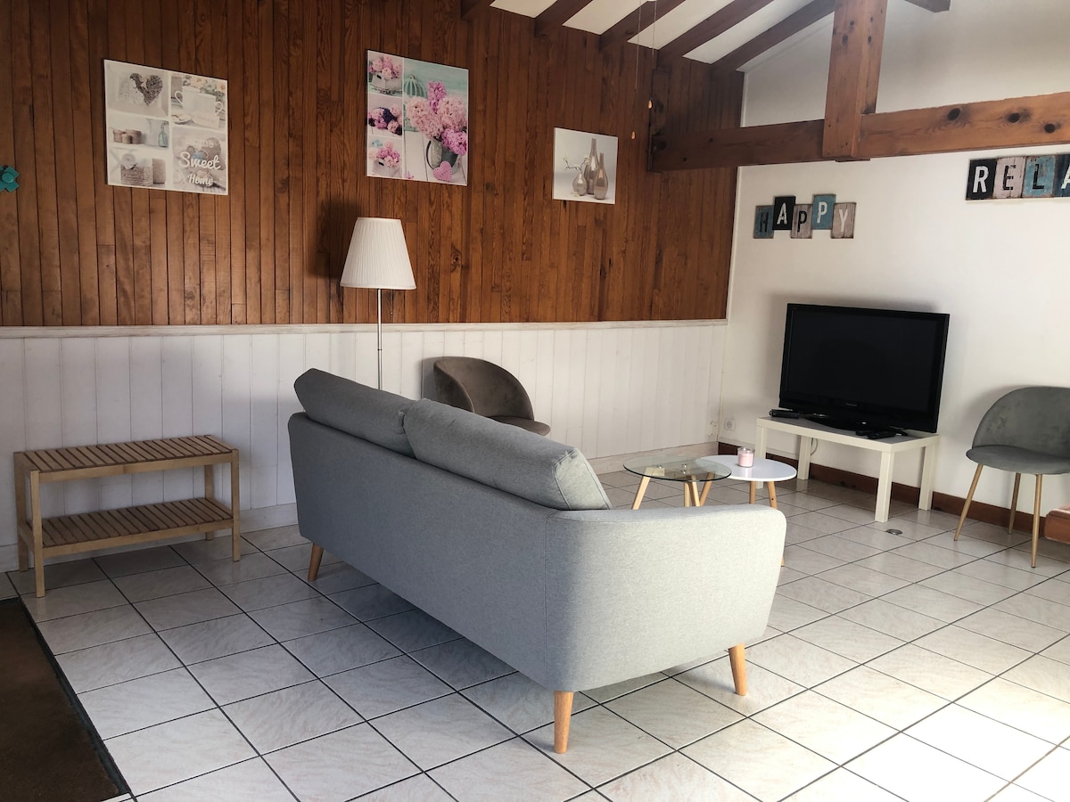 A spacious living area is featured, showcasing a grey sofa and a glass coffee table. A modern television is positioned on a low cabinet. Light-colored walls and wooden paneling create a warm ambiance, complemented by decorative wall art and a standing lamp.