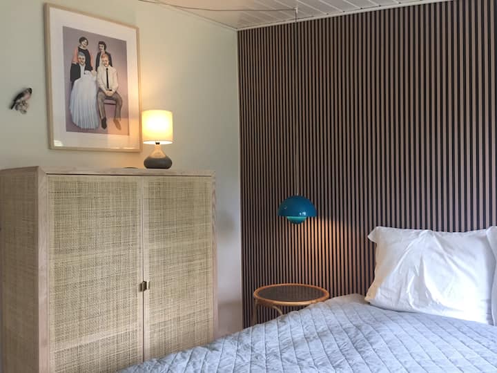 Bright bedroom with two windows facing the garden. One to the south and one to the east, so there is morning sun. Decorated with a stove-table bed of 150cm and a smaller closet. One wall has striped wallpaper in brown and pink that adds warmth and personality.