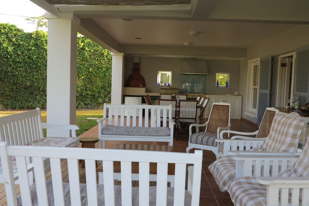 An outside covered patio. seating on benches and couches as well as a 12 seater table. Gas barbeque