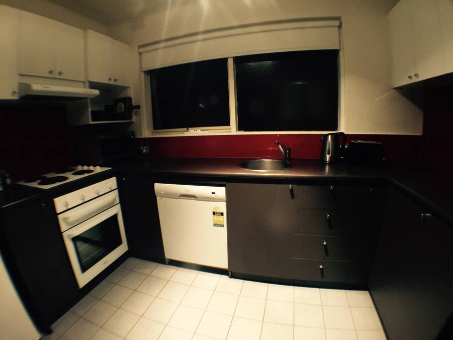 Kitchen area with fridge, dishwasher, electric oven and cooktop, microwave, kettle, toaster and other essential kitchen utensils.