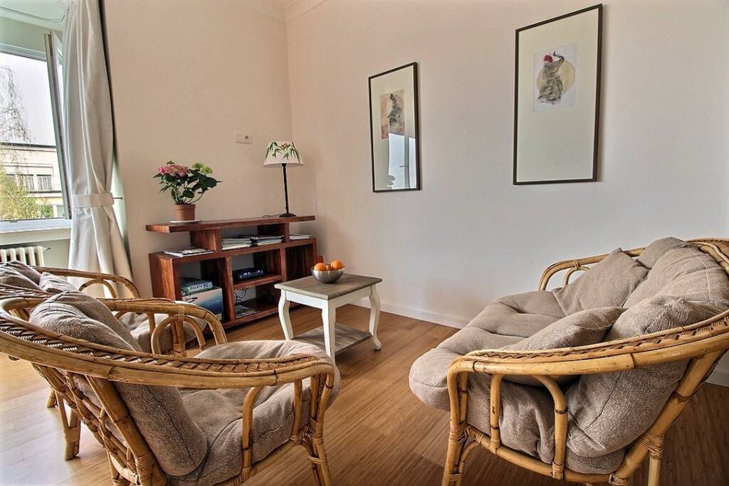 Détail du coin salon avec tableaux, étagère et fauteuils et canapé en osier.