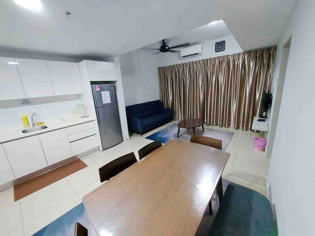 A modern kitchen area features sleek cabinetry and a refrigerator, complemented by a dining table surrounded by chairs. A comfortable three-seater sofa is positioned near large windows, adorned with curtains. A ceiling fan is visible, contributing to the airy ambiance.