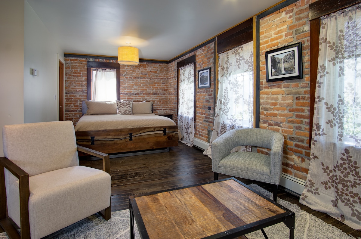 חדר שינה מס '1 בקומת הקרקע עם מיטת עץ בגודל קינג סייז, פינת ישיבה פרטית וטלוויזיה.  מוקף בקירות לבנים ורצפות עץ מקוריות משנת 1905