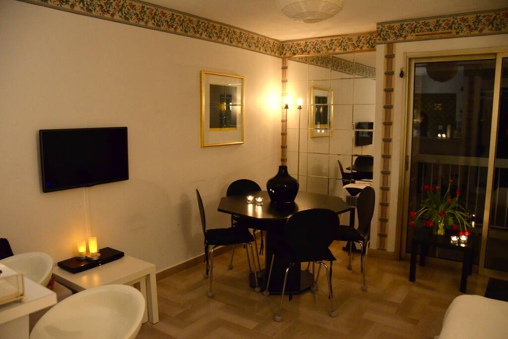 Living room with A/C as seen when entering the apartment with sofa bed, flatscreen TV and dining table with four chairs. Access to the balcony from here via double doors with electrical shutters.