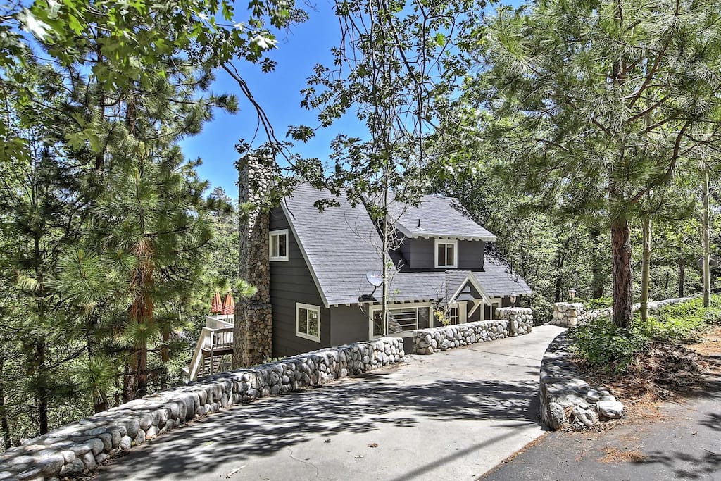 The lovely cottage is tucked below a rock wall and surrounded by towering trees.