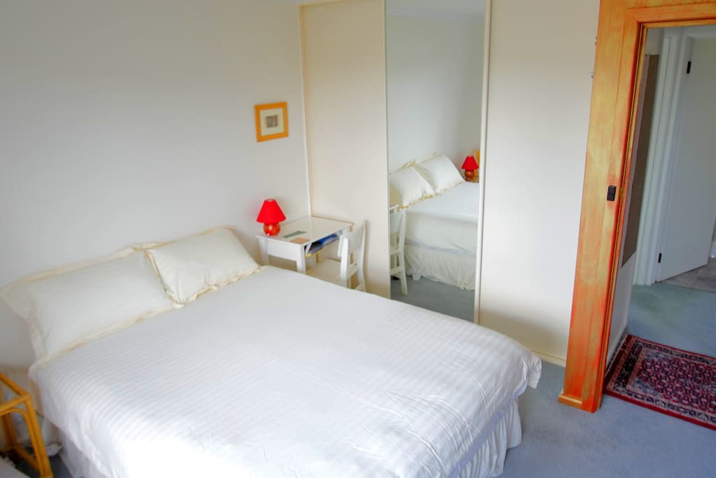 A Queen sized bed in a room with built in wardrobe including ceiling to floor length mirror