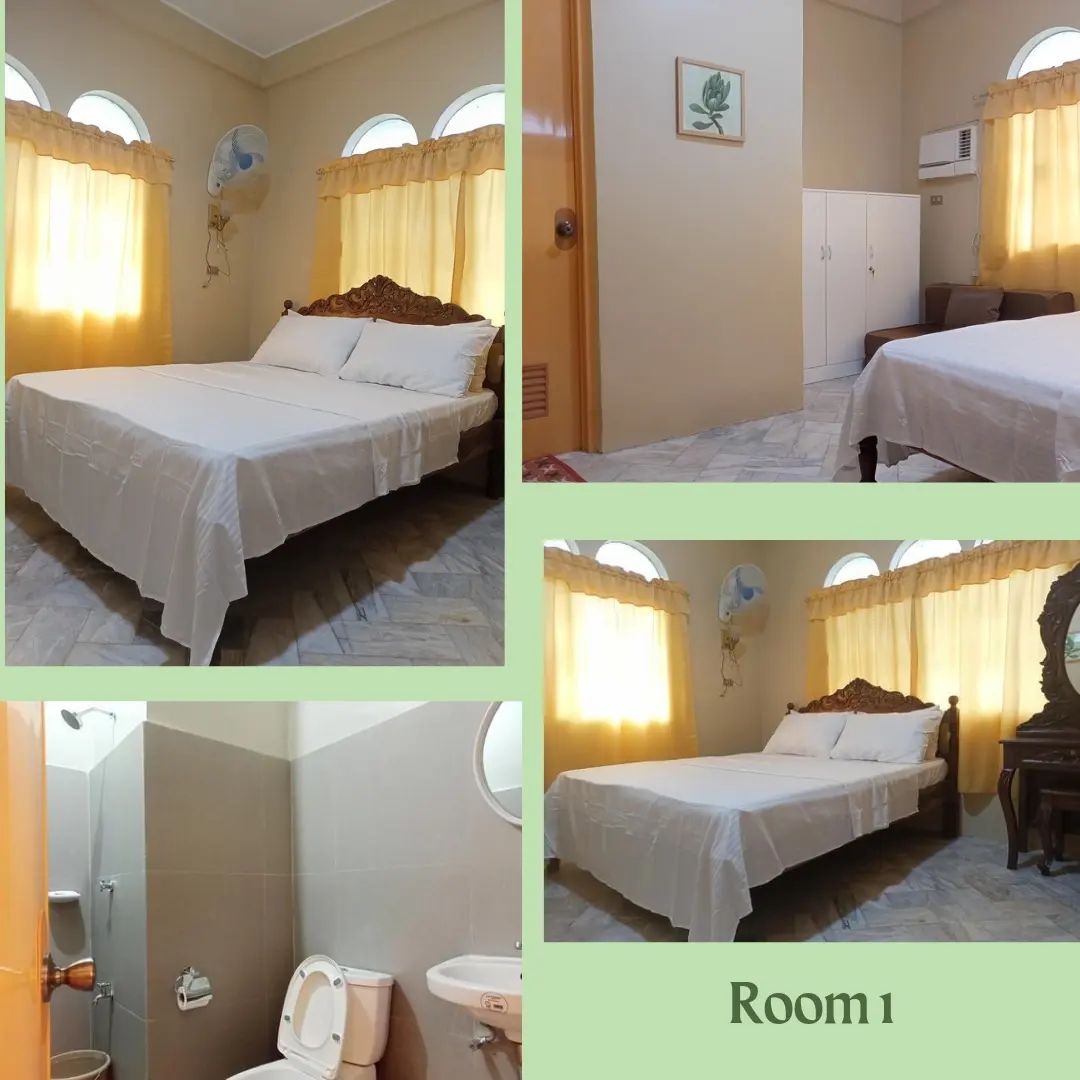 The room features a spacious bed with a white coverlet, soft lighting from large windows dressed in light curtains. A compact wardrobe and a cozy chair are included. An adjoining bathroom is visible, showcasing modern fixtures and a clean, minimal design.