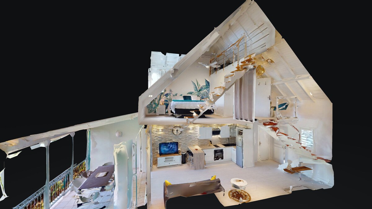 A multi-level apartment showcases an open-concept living area with a cozy seating arrangement and a connected dining space. A well-equipped kitchen is visible, along with a staircase leading to an upper sleeping area. Natural light floods the space through large windows.