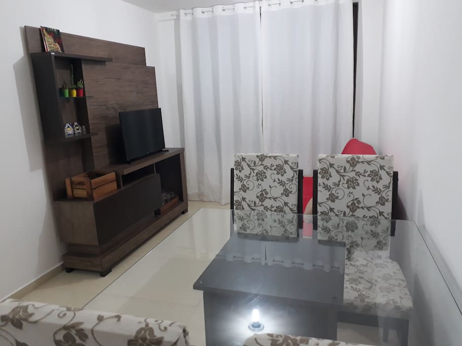 Sala: mesa com 4 cadeiras, sofá-cama e rack-estante com TV 32 polegadas