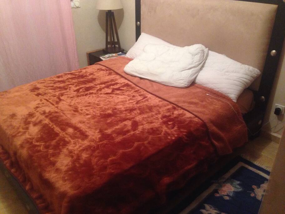 Le lit deux places de la chambre du voyageur avec couverture , drap et placard pour rangement .