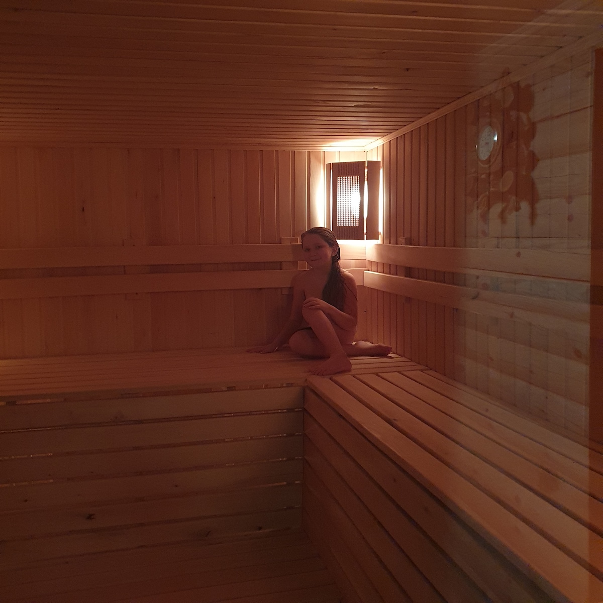 A wooden sauna interior is presented, featuring smooth bench seating arranged in a tiered layout. Warm, soft lighting enhances the natural wood tones, creating a tranquil environment. The image conveys a peaceful setting for relaxation.