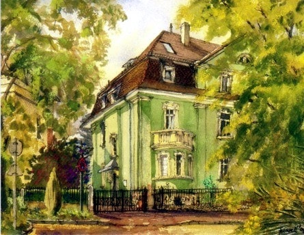 A charming green villa, set amidst lush foliage, displays a classic architectural style. The building features a balcony and white window trim, surrounded by well-kept gardens and a wrought-iron fence. Street signs and mature trees contribute to the serene atmosphere.