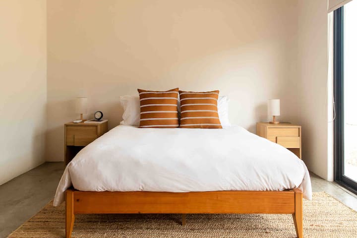 Chambre secondaire avec un lit queen et un matelas hybride. Des stores occultants et une porte coulissante vers l'extérieur. Climatiseur dans la chambre.