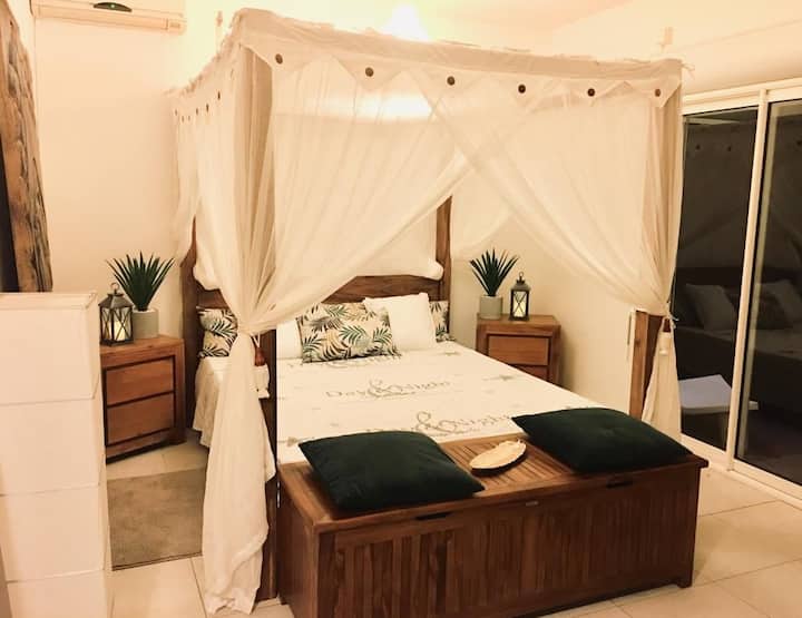 L 'espace nuit avec un grand lit double baldaquin en bois de Bali et sa moustiquaire sur mesure.