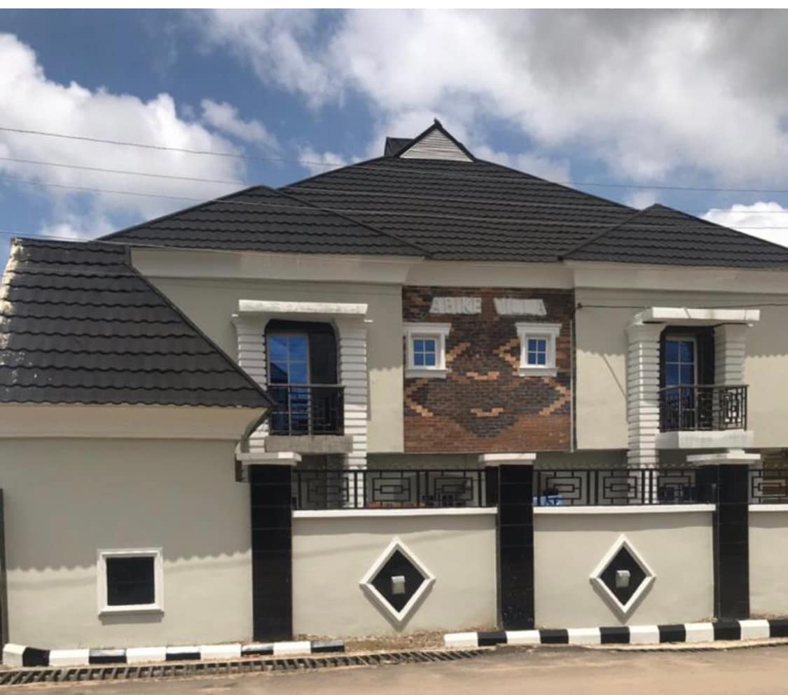 A contemporary holiday home is showcased with a modern architectural design. The building features a dark, tiled roof and striking brick accents. Decorative elements include diamond-shaped window frames and railings, with large windows allowing natural light to enter.