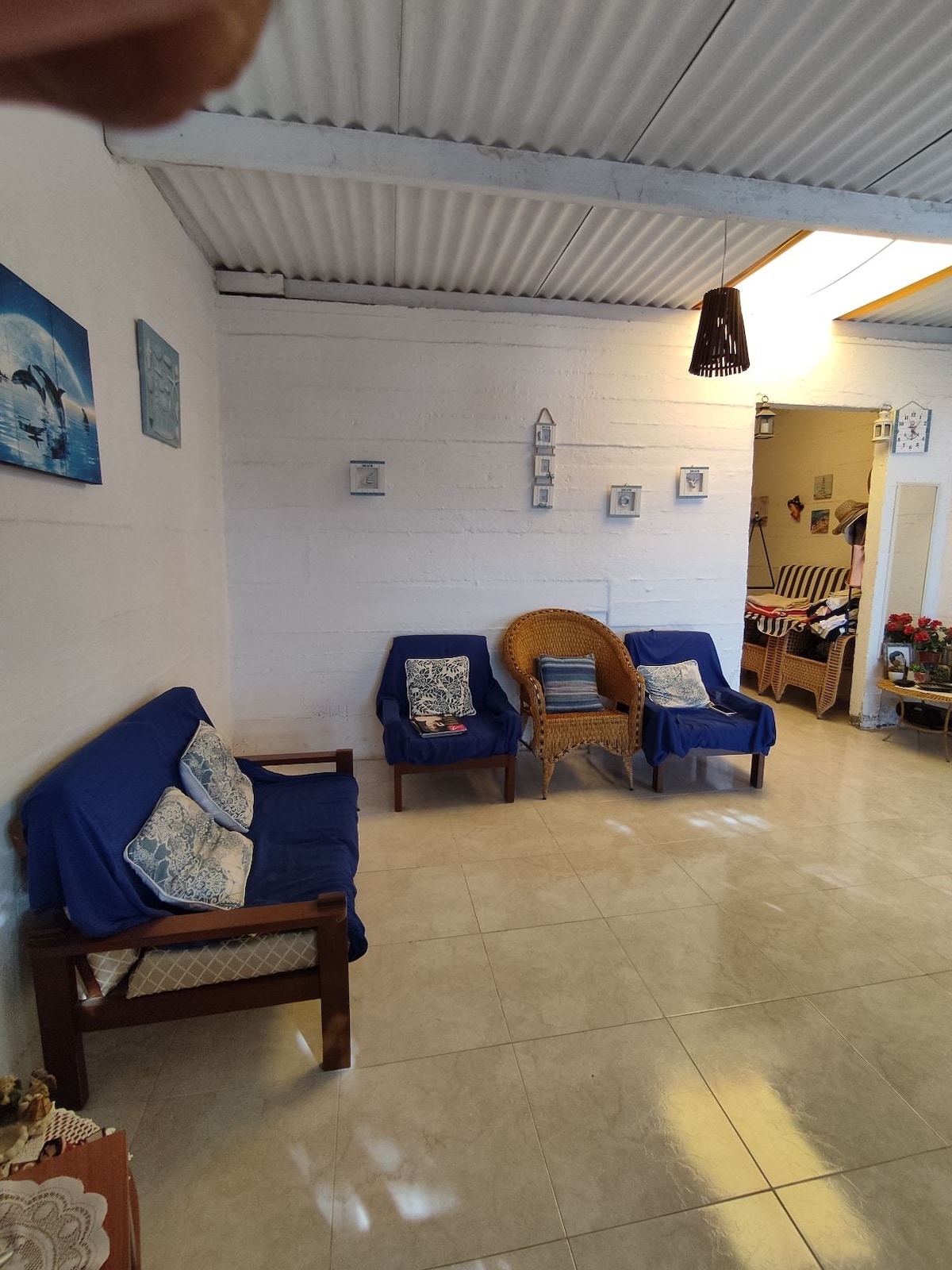 A cozy living area features two blue-upholstered chairs and a matching sofa, complemented by decorative cushions. Light-colored walls and tiled flooring enhance the spacious feel. Decorative wall art adds character, while a doorway leads to another part of the house.