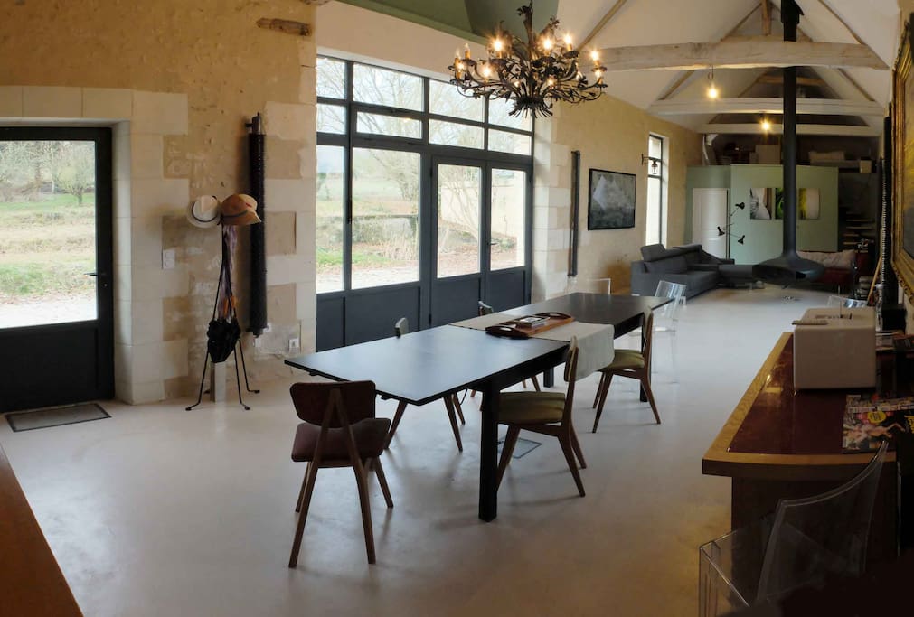 view of the main living room, seen from the entrance to the kitchen. There is a small breakfast table, a few comfortable sofas around a modern designer fireplace. In the background you can see the mezzanine with a library, an artists workspace and a clic clack sofa bed