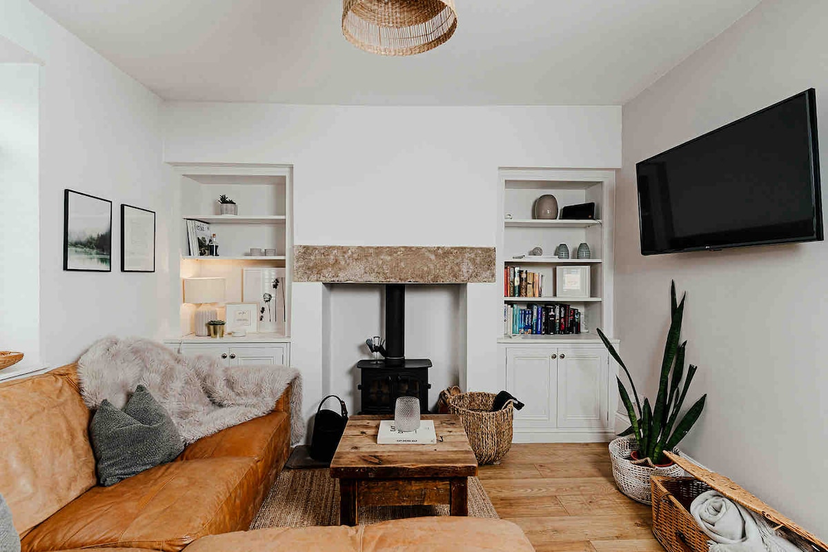 The lounge features a leather sofa accented with plush throws, paired with a wooden coffee table. A stone fireplace serves as a focal point, flanked by built-in shelves displaying books and decorative items. A wall-mounted TV is positioned for relaxation.