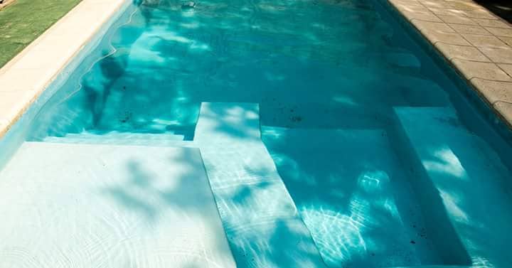 A shared swimming pool measuring 4m x 9m is visible, featuring a light blue bottom and steps leading into the water. The clear water reflects greenery and sunlight, creating a refreshing ambiance. Surrounding areas include tiled flooring and shaded sections.