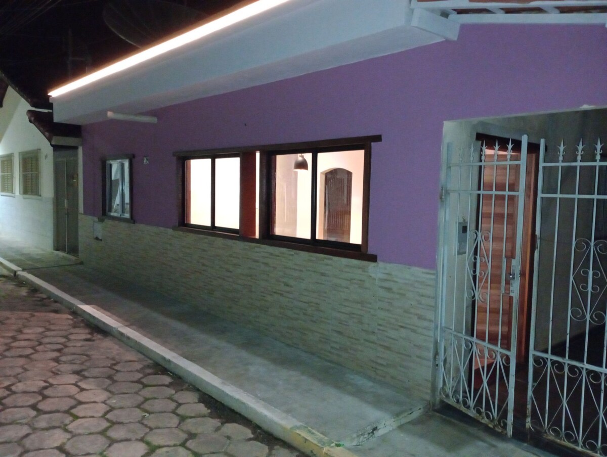 The exterior of the property features a vibrant purple wall complemented by a light-colored stone base. Large windows allow for natural light to illuminate the interior space, while a decorative gate adds an element of charm to the entrance.