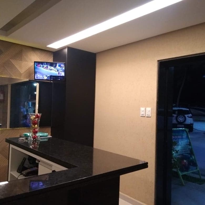 A sleek reception area is displayed, featuring a dark polished countertop and a wall-mounted television displaying footage. Decorative items, including a glass vase filled with colorful objects, are positioned on the counter, while a doorway leads to an outdoor view.