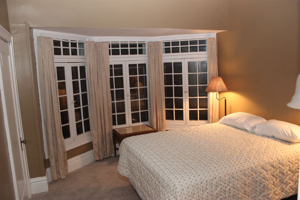 The bedroom has a large bay of french casement windows and a queen-size bed.