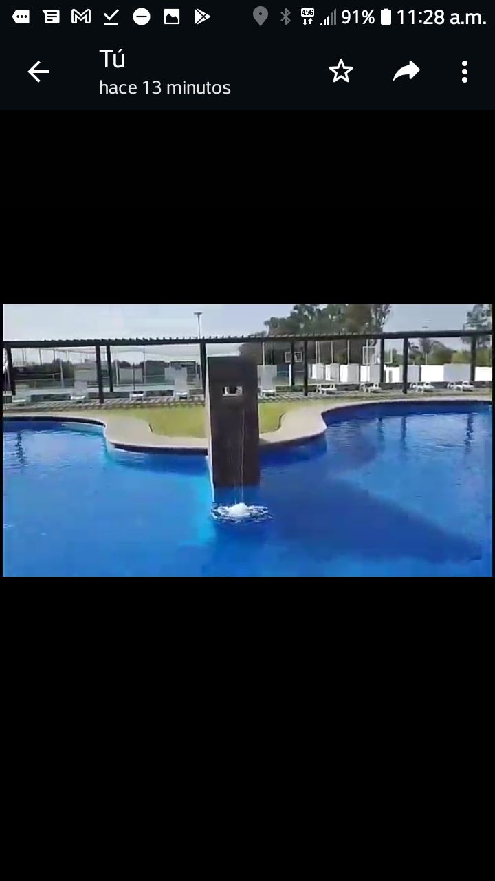 A large swimming pool is visible, featuring a central waterfall that creates a gentle cascade into the water. Surrounding the pool, green grass and shaded lounging areas enhance the inviting environment for relaxation.