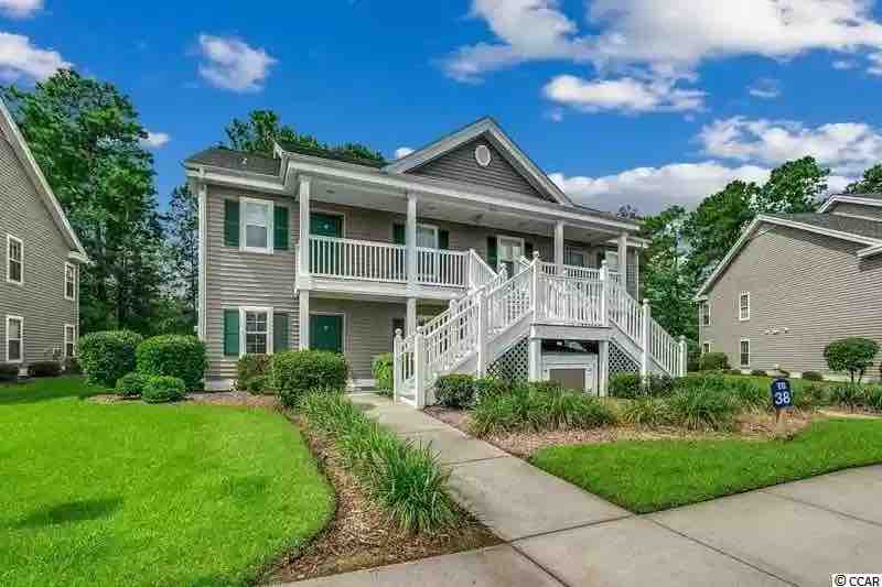 The exterior showcases a well-maintained, two-story building in a soft gray tone, framed by lush greenery and manicured landscaping. A wide staircase leads to the welcoming entrance, with a covered porch accentuated by white railings and inviting double doors.