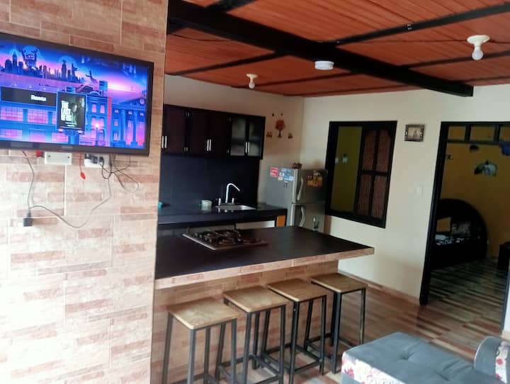 Vista desde la puerta de la entrada principal del apartamento que tiene de fondo la habitación auxiliar con Cama nido y en esta foto se ve el mesón de la cocina y mesón de comedor tipo barra americana