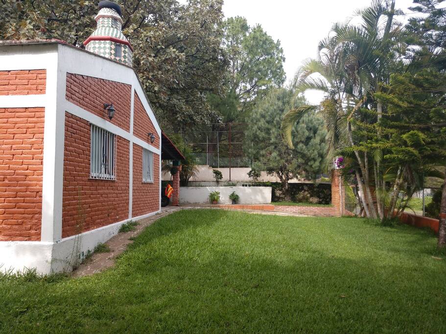 Jardín espacioso al frente de la cabaña dando hacia la calle empedrada Rosa Morada