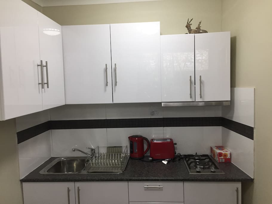 Kitchen with appliances, cooktop, fridge, microwave, cutlery, bowls, plates, pots and pans. Also includes oil, sugar, tea, salt and pepper.