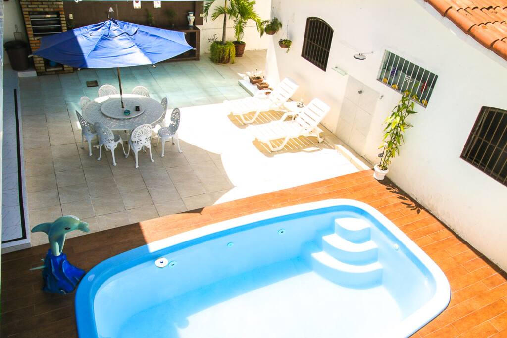 Área externa com piscina, churrasqueira, mesa, cadeiras, espreguiçadeiras e geladeiras disponíveis.