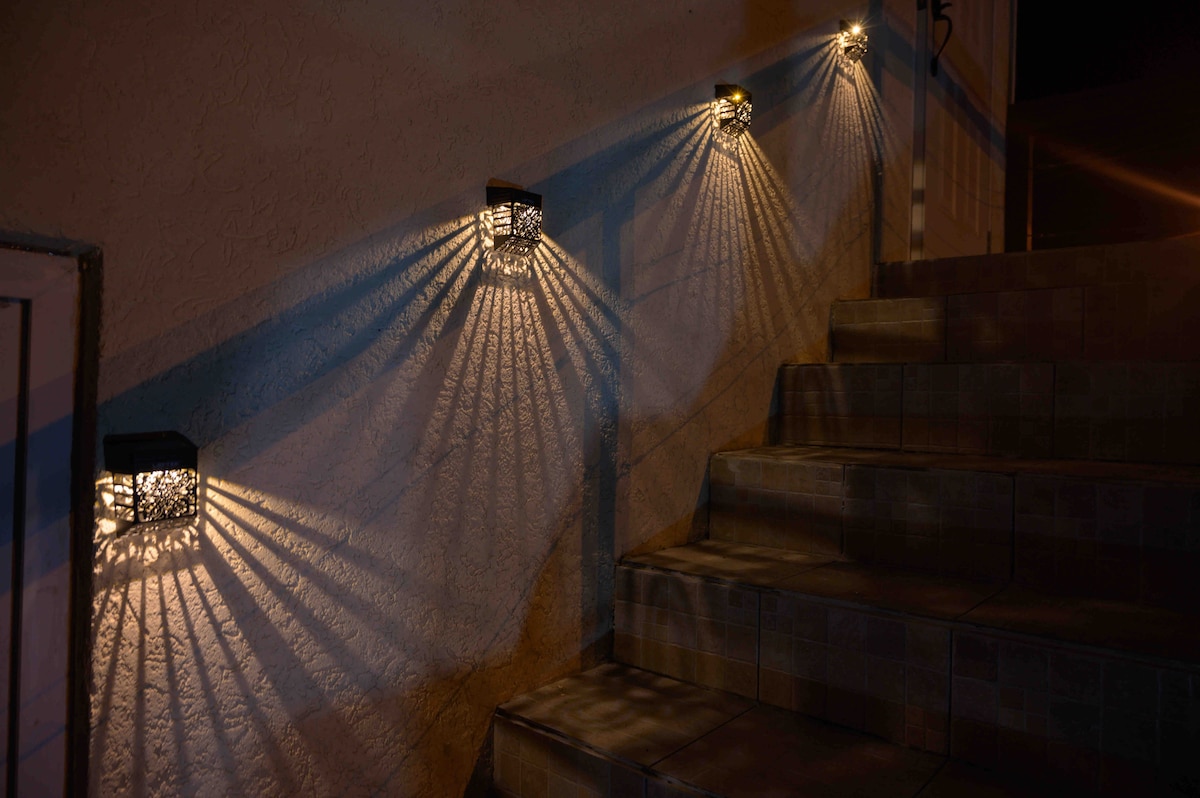 An inviting staircase is illuminated by decorative wall lights, casting intricate shadows on the steps. The warm light enhances the welcoming appearance of the entrance, guiding guests safely as they ascend.