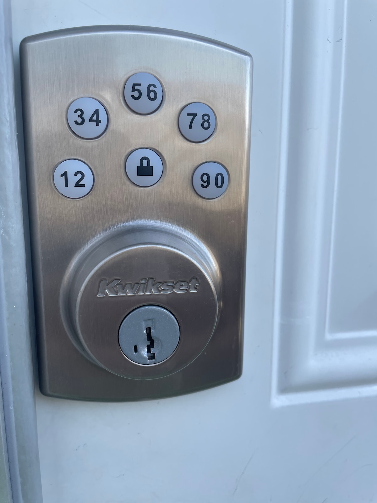 A Kwikset keyless entry lock is mounted on a light-colored door. The lock features a keypad with numbered buttons and a keyhole. The overall design is sleek and modern, enhancing accessibility for guests upon arrival.