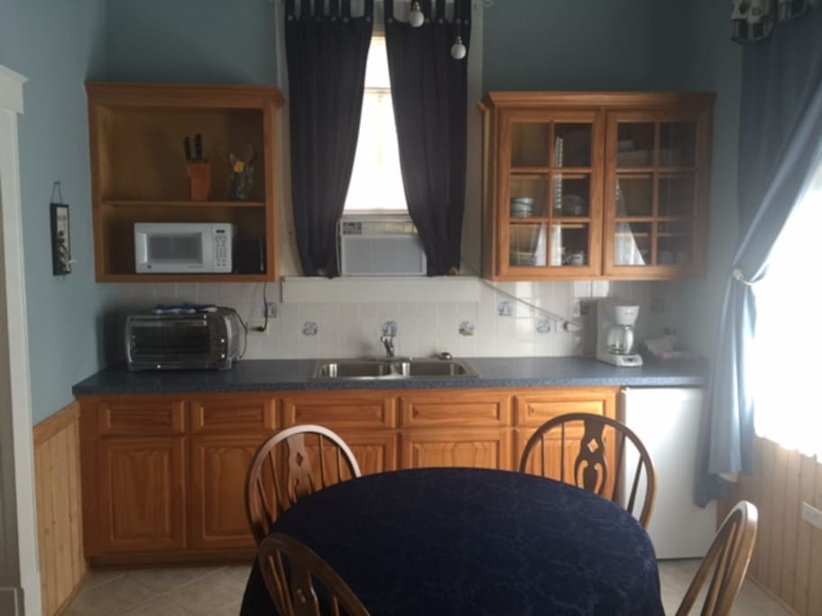 Small kitchen with microwave, toaster oven, coffee pot, fridge, dishes, etc.