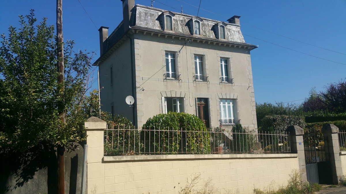 The exterior of the house features a classic architectural style with a light-colored facade. The structure has multiple windows adorned with shutters, and a well-maintained garden with greenery surrounds the entrance. A fenced area enhances privacy, creating a welcoming first impression.