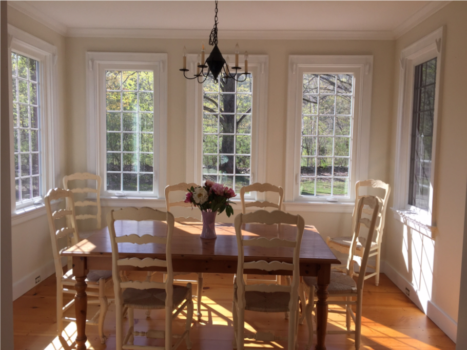 Bright and sunny dining room with windows on three sides and door to one of two porches, seats 8 plus 4 at kitchen island bar