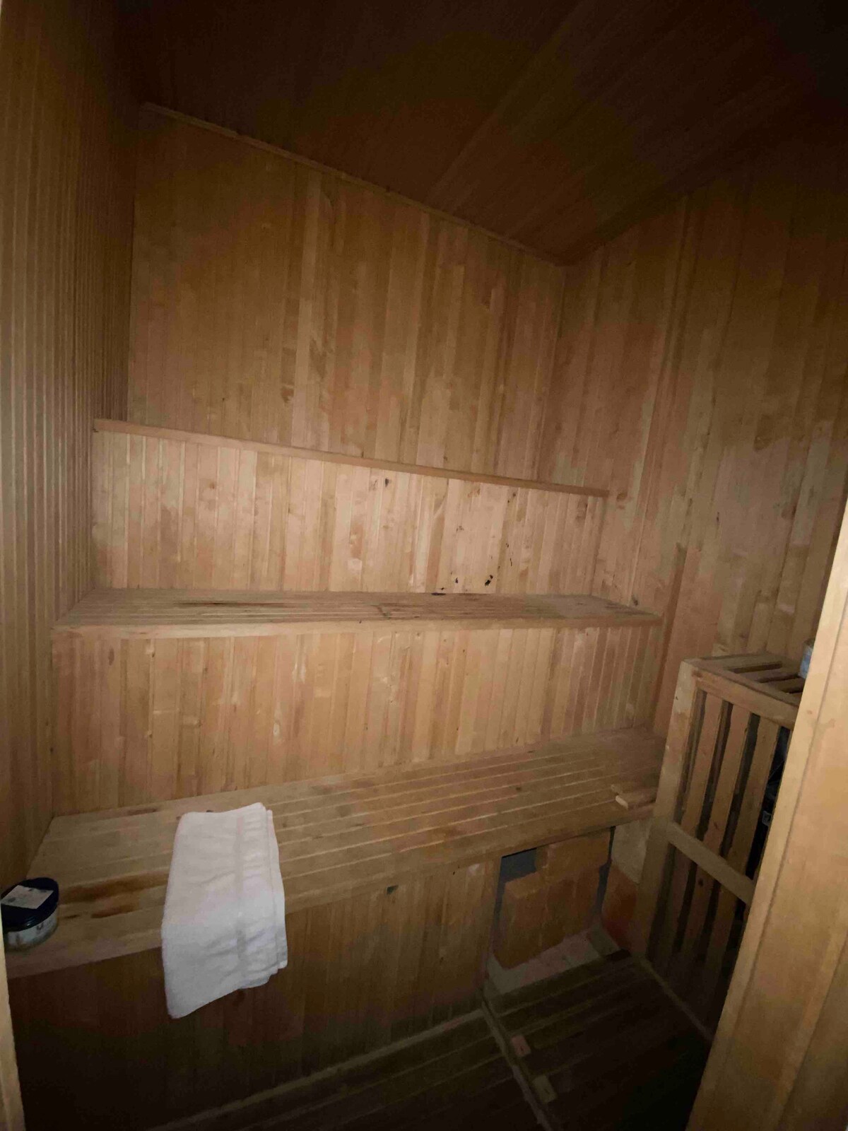 A wooden sauna features smooth, warm-toned planks lining the walls and benches. Several shelves are visible, providing space for towels or personal items. A neatly folded towel sits on the lower bench, adding a touch of convenience. Soft lighting enhances the intimate atmosphere.