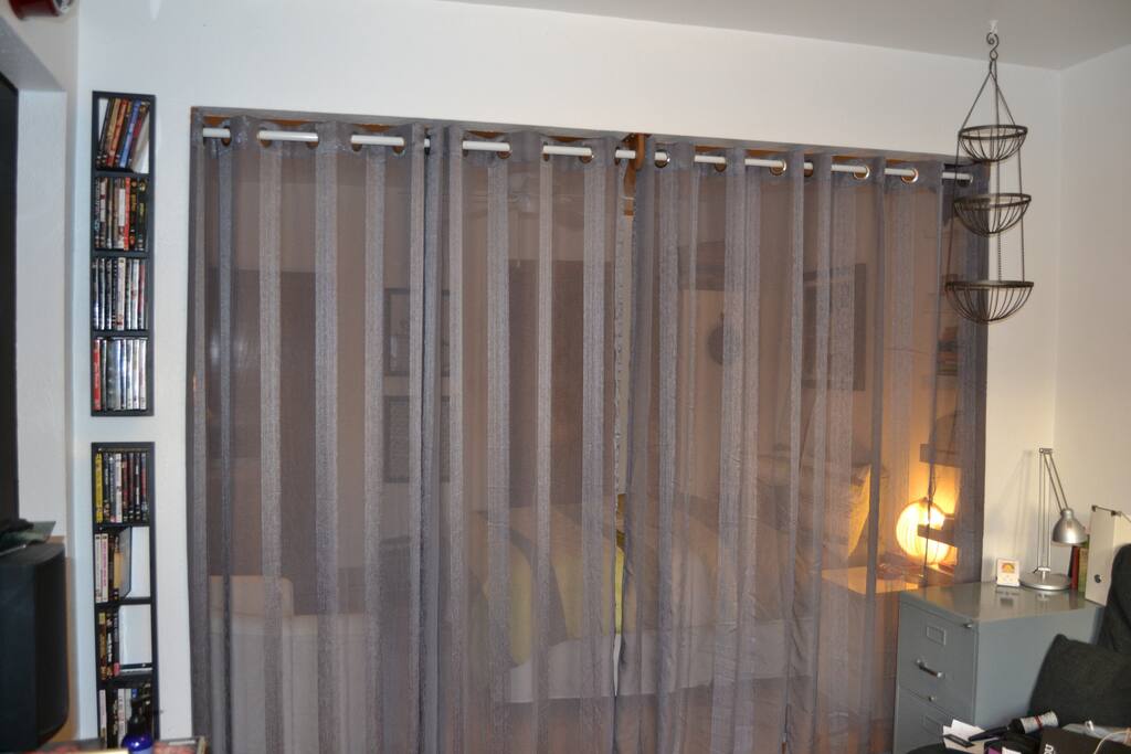 La chambre est séparée du salon par un voilage gris/ A curtain separates the bedroom from the living-room