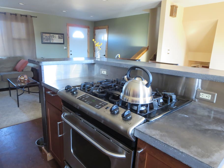 Stainless gas range, concrete counter kitchen island.