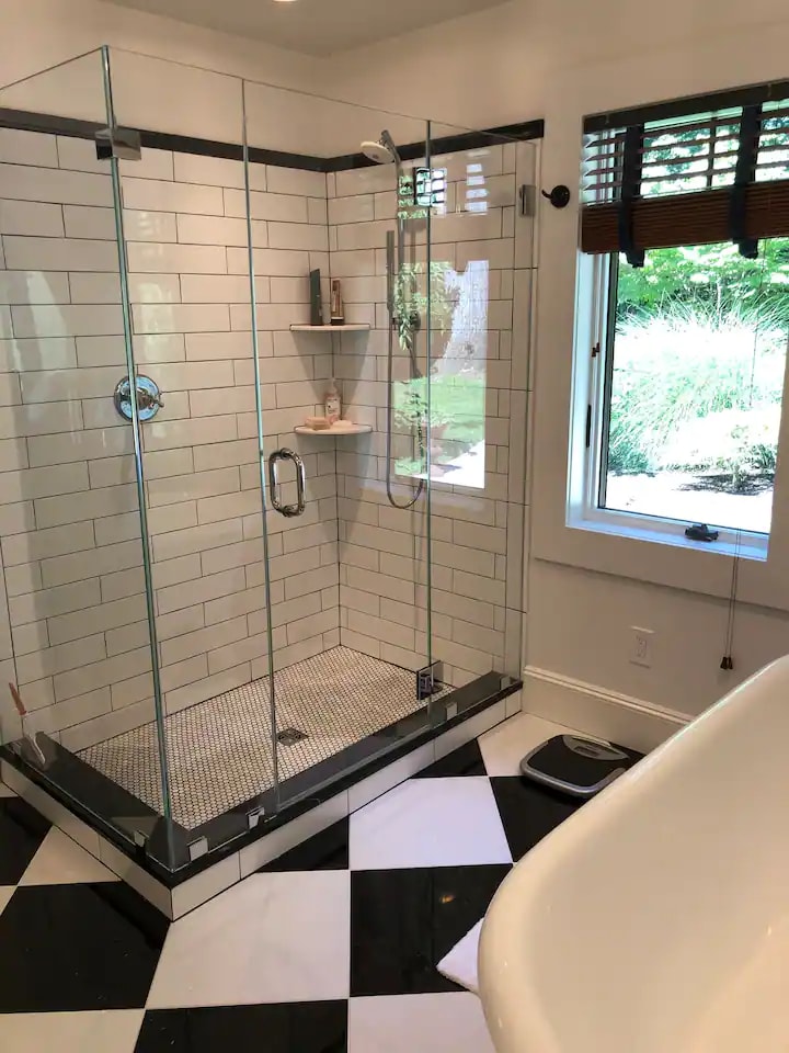 A modern bathroom features a frameless glass shower with sleek tile accents and a light-filled window. A spacious bathtub stands near the shower, complemented by a striking black and white tiled floor that enhances the overall design.