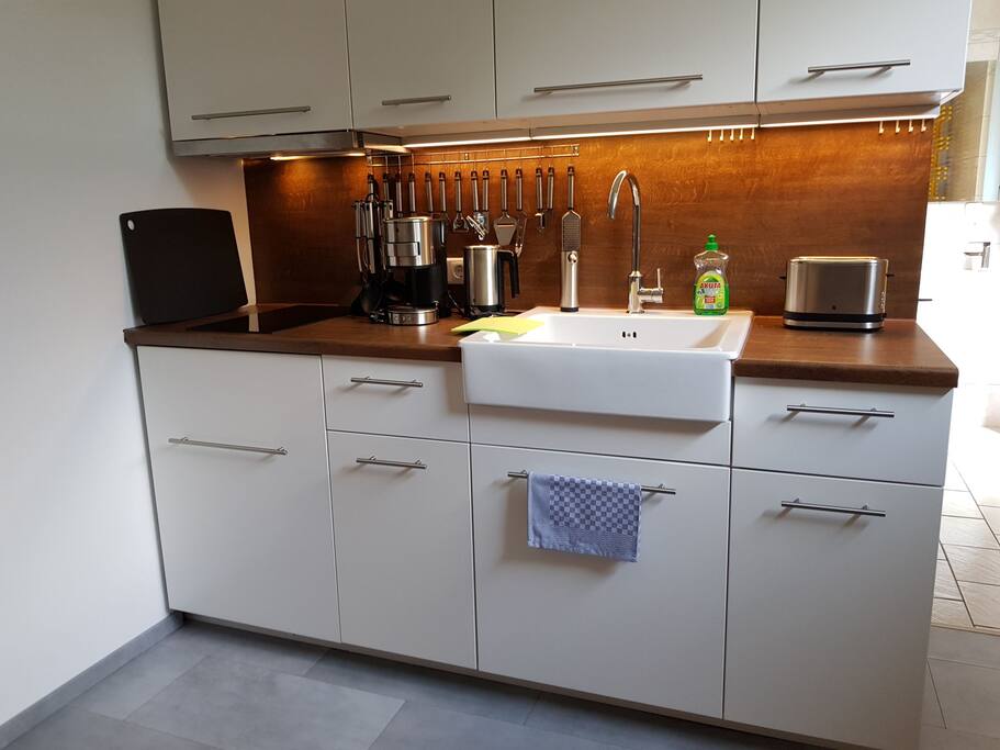 Küchenzeile mit Kühlschrank, Kochfeld, Waschbecken, Küchenutensilien, Wasserkocher, Schneidebrett, Kaffeepad-Maschine, Mikrowelle mit Grill und Toaster