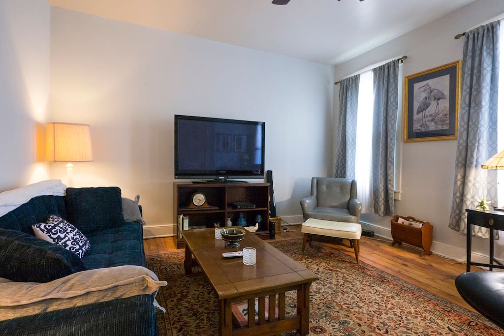 Another view of living room with refinished pine wood floors and big screen TV. Room has 3 tall windows .