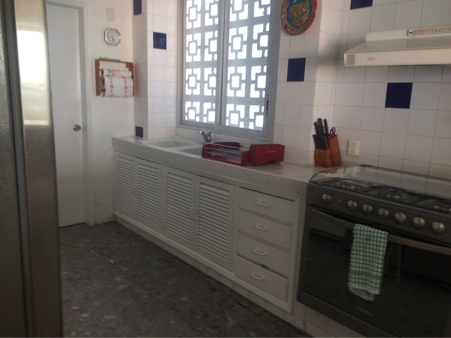 Cocina equipada con microondas, refrigerador, estufa de gas, horno de gas, hornito eléctrico, cubiertos, platos y vasos.